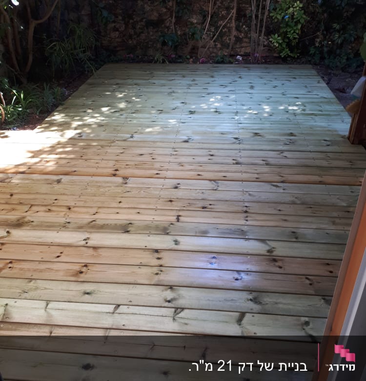 דק עץ חדש בגינה עם צמחייה מסביב